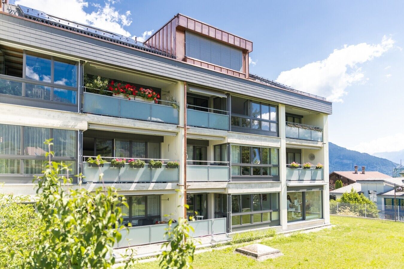 Un edificio de varios pisos con balcones, ventanas amplias y un área verde en la parte frontal.