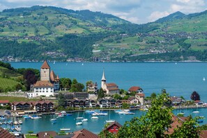 Un pueblo a orillas de un lago, con una iglesia destacada, un puerto deportivo con barcos y colinas verdes circundantes.