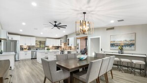 A modern kitchen with white cabinets, a large island, and a dining area with a wooden table and gray chairs. - Scenic West Sedona Escape with Thunder Mtn Views (Sedona)