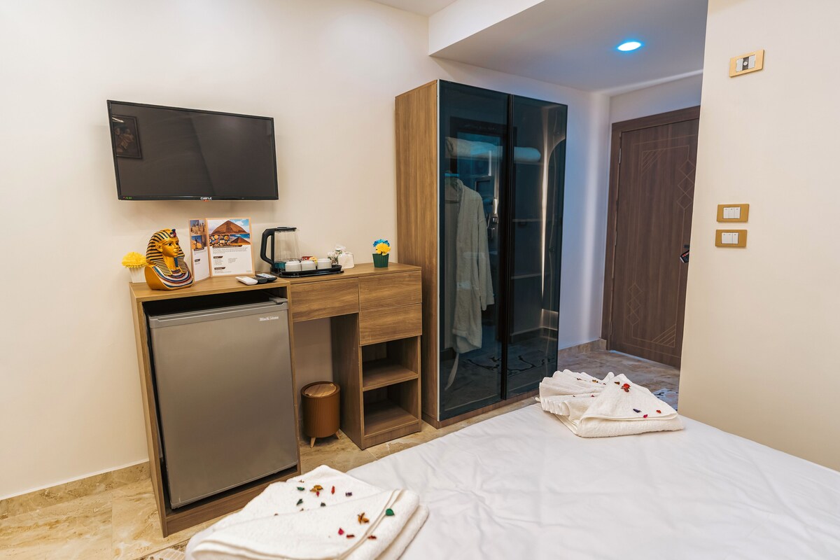 A hotel room with a bed, a desk with a television, a minibar, and a wardrobe.