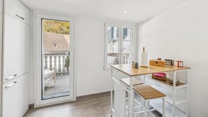 A small, bright kitchen with white cabinets, a wooden table, and a view of a garden through a glass door.
