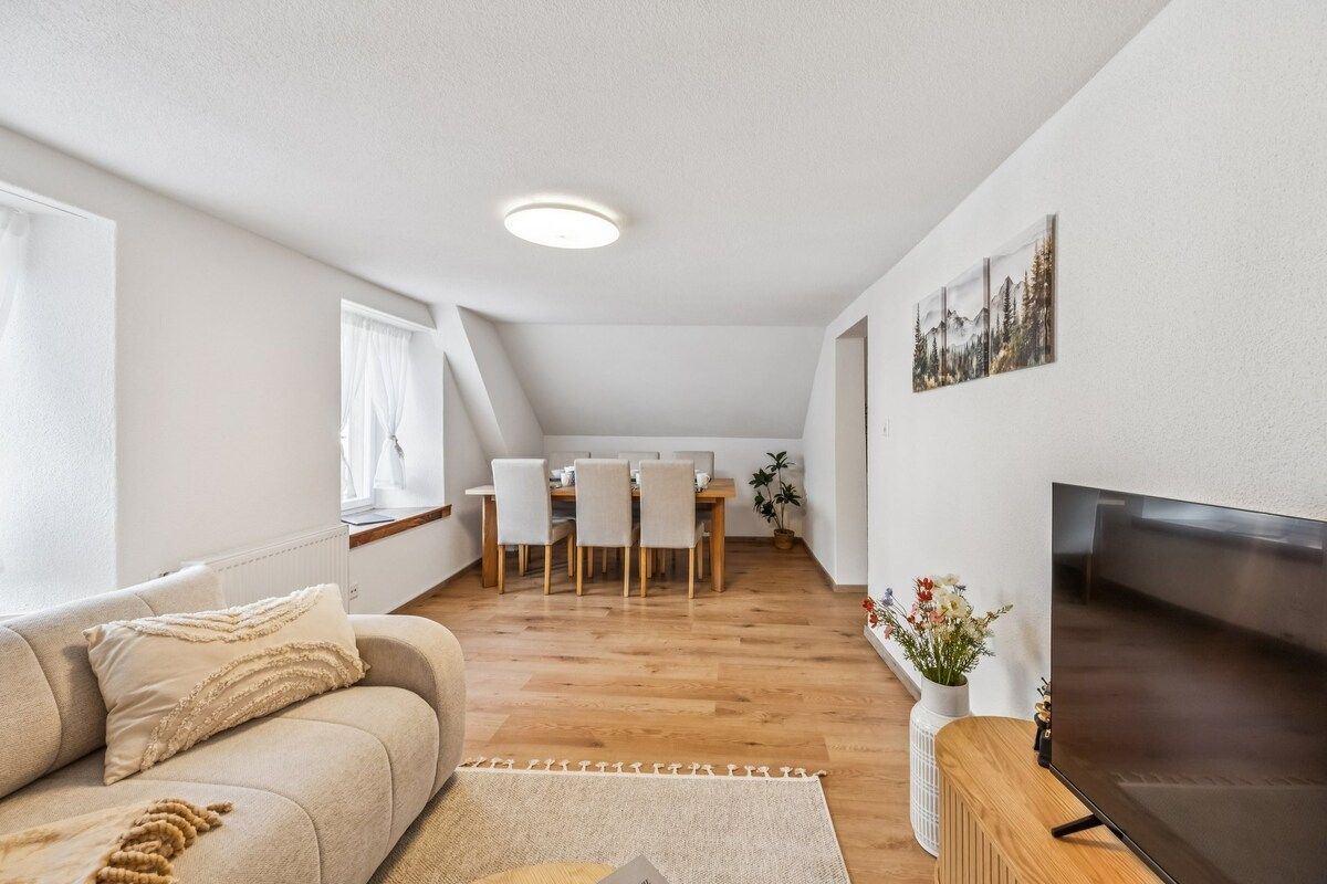 Ein modernes Wohnzimmer mit einer Couch, einem Flachbildfernseher und einem Essbereich mit Tisch und Stühlen.