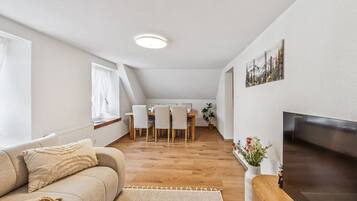 Ein modernes Wohnzimmer mit einer Couch, einem Flachbildfernseher und einem Essbereich mit Tisch und Stühlen.