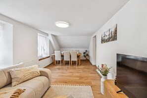 Un salon moderne comprenant un canapé, un téléviseur à écran plat et un coin repas avec une table et des chaises.