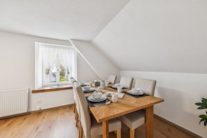 A dining area with a wooden table set for six, white curtains on a window, and a white radiator.