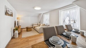A modern, well-lit room with a sofa, dining table set for four, and a large window with curtains.