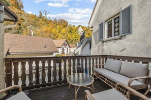 Un balcón con sofá de mimbre, una mesita redonda y vistas a casas y árboles.