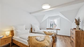 Quarto de hotel com duas camas, cômoda de madeira, mesa de cabeceira e janela com cortinas.