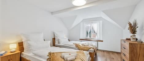 Una camera d'albergo con due letti, una cassettiera in legno, un comodino e una finestra con tende.