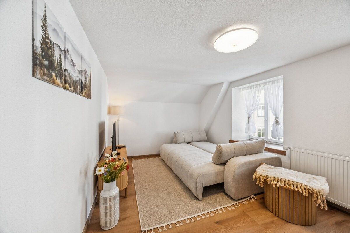 Une chambre confortable avec un lit, une table de chevet avec une lampe, une fenêtre avec des rideaux et un tableau accroché au mur.