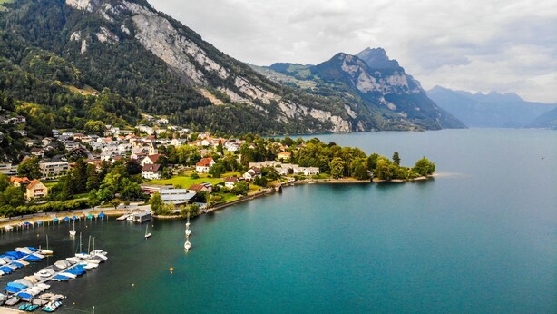 A lakeside town with houses, a marina, and mountains in the background.
