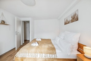 Une chambre à coucher avec un lit en bois, une literie blanche, un plaid beige et une lampe de chevet.