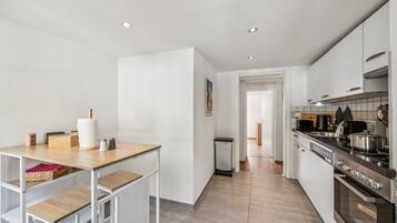 A modern kitchen with white cabinetry, a stainless steel stove, and a wooden table with kitchen items.