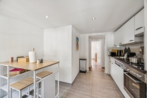 A modern kitchen with white cabinetry, a stainless steel stove, and a wooden table with kitchen items.
