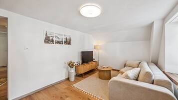 Un salon moderne avec un canapé, une table basse, un téléviseur posé sur un meuble en bois et une lampe.