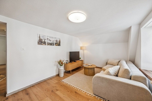 A modern living room with a sofa, a coffee table, a TV on a wooden cabinet, and a lamp.