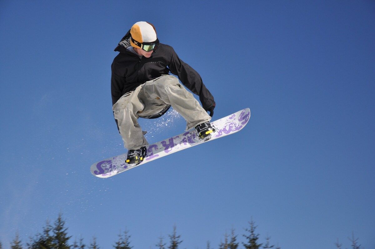Eine Person snowboardet in der Luft vor blauem Himmel.