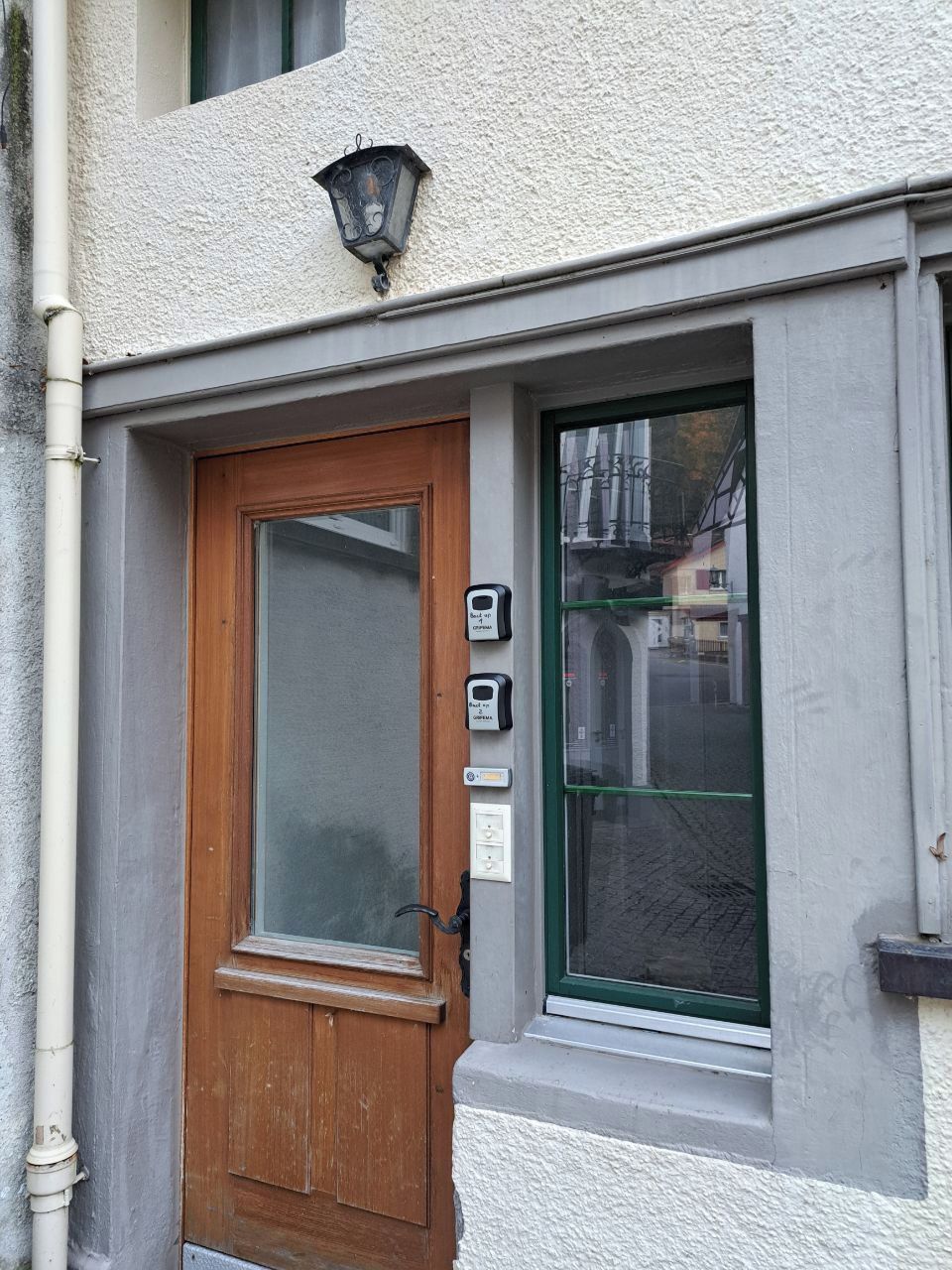 Une porte en bois avec un panneau en verre dépoli, une petite fenêtre à cadre vert et un luminaire fixé au mur.