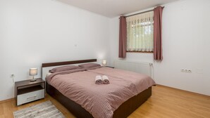Un dormitori amb un llit, taules de nit, un radiador i una finestra amb cortines.