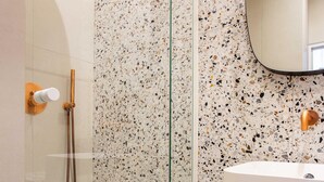 A modern bathroom with a glass-enclosed shower, a white sink, and a speckled tile backsplash. - Authentic Apartment in Paris (Paris)