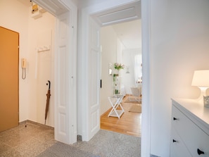 A hallway with a wooden door, a white wall-mounted phone, a black umbrella, a white folding chair, and a white desk with drawers. - Arcadio Home - Junior Suite (Graz)