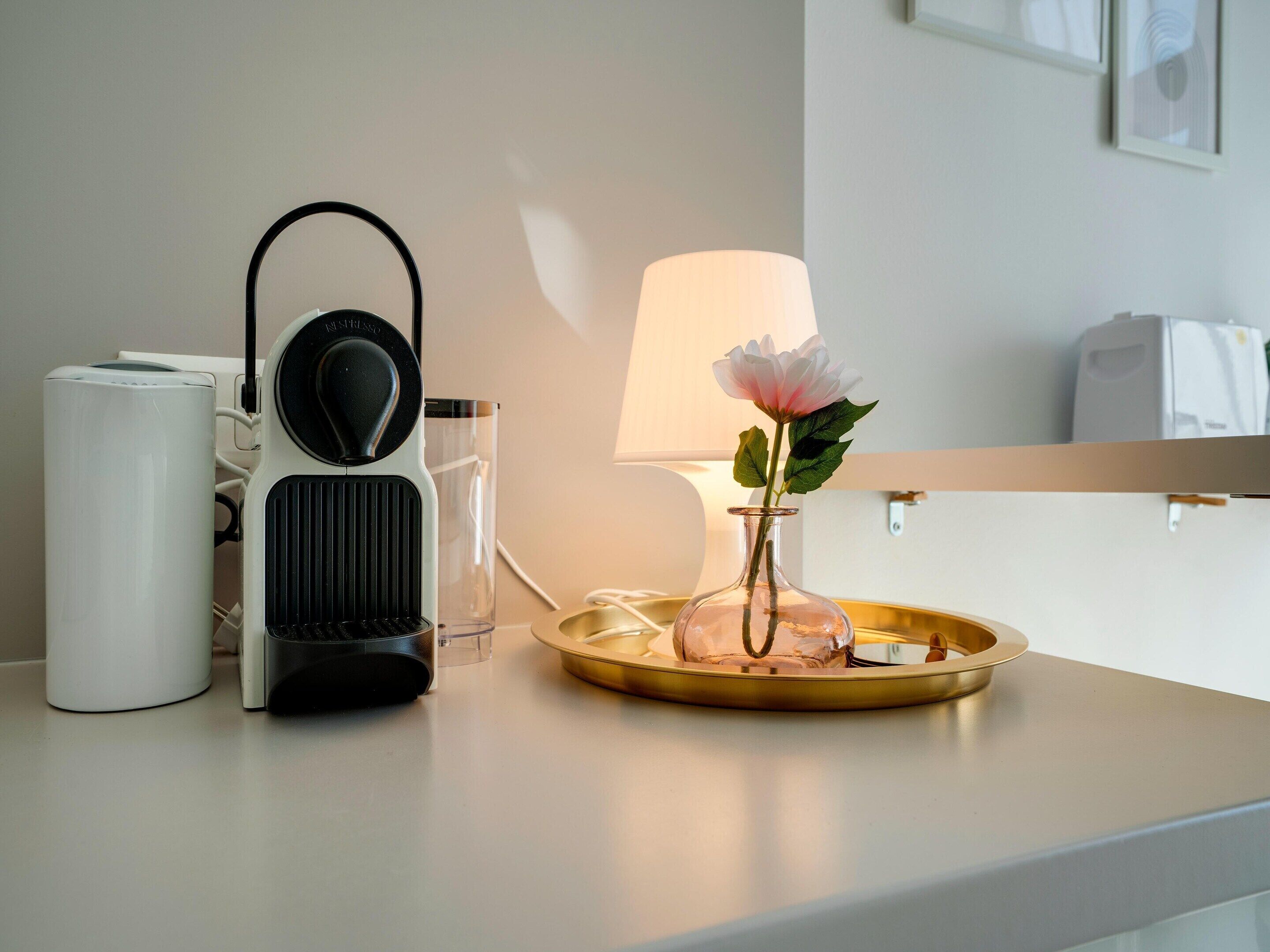 A modern kitchen with a coffee maker, a glass vase with a flower, and a lamp on the counter.