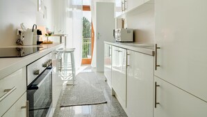 A modern kitchen with white cabinetry, a built-in oven, and a small island with stools. - Arcadio Home - Junior Suite (Graz)