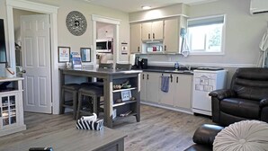 A modern kitchen with white cabinets, a central island, and a dining area with a couch and chairs. - Tiny Home| Full Kitchen | Sleeps 4 + Work Desk. Relax, explore Acadian Peninsula (Allardville Parish)