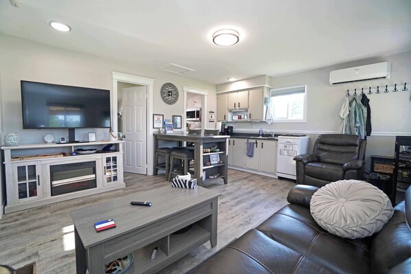 A modern living room with a flat-screen TV, a fireplace, a dining area, and a kitchen.