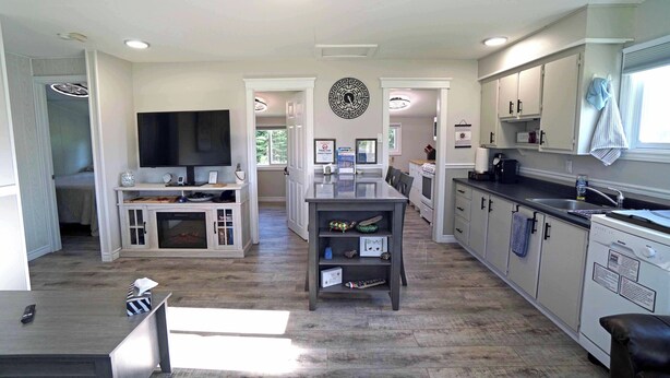 A modern kitchen with white cabinets, a central island, and a dining area with a TV. - Tiny Home| Full Kitchen | Sleeps 4 + Work Desk. Relax, explore Acadian Peninsula (Allardville Parish)