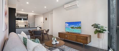 Uma sala de estar moderna com sofá, mesa de centro, televisão e área de jantar com cadeiras e mesa.