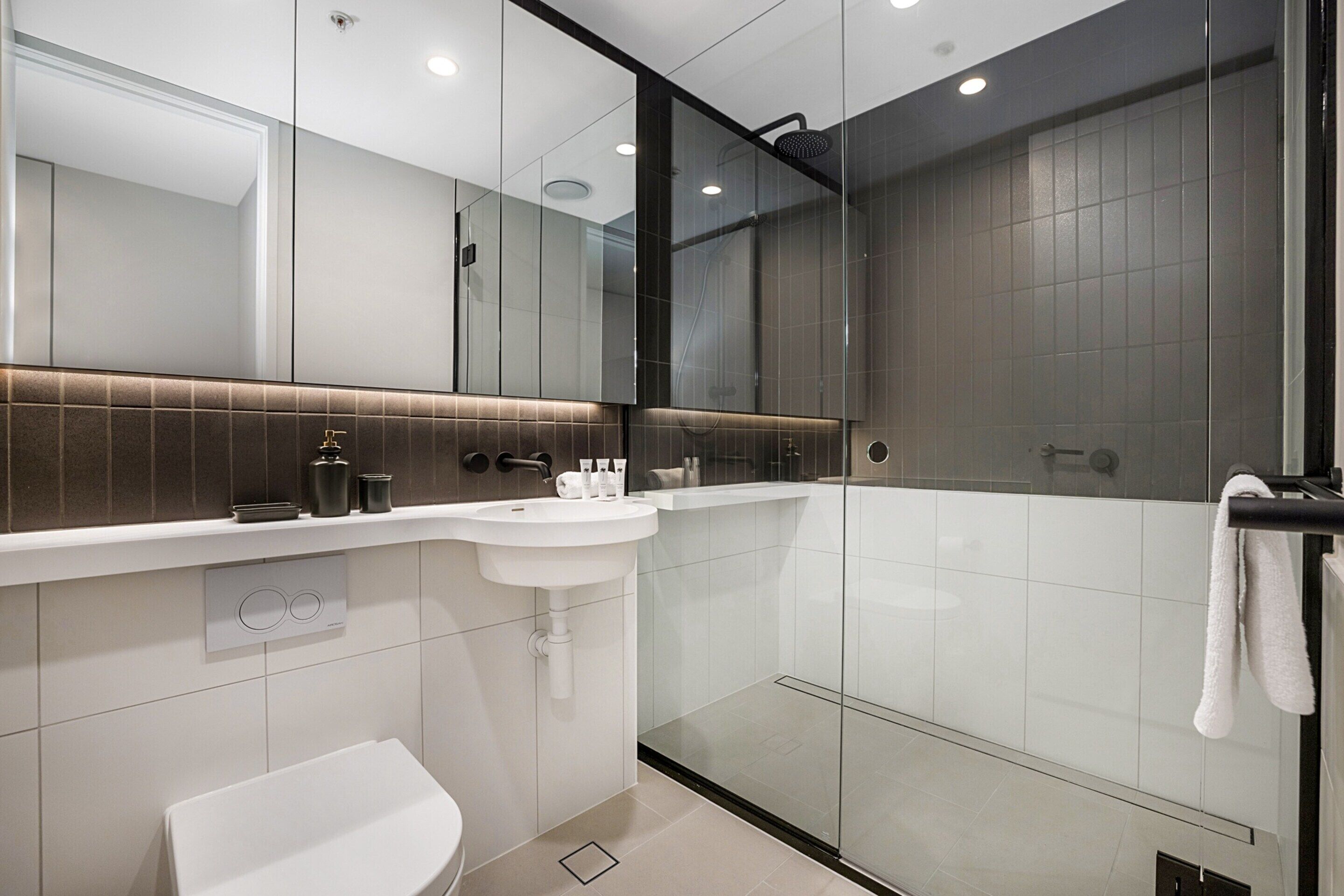 Un bagno moderno con cabina doccia in vetro, un lavandino bianco e uno specchio grande.