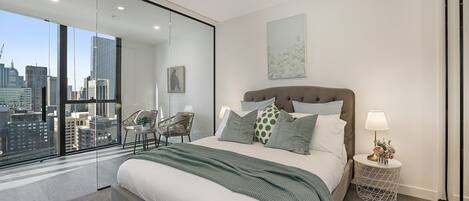 A modern bedroom with a large bed, city view, and a glass partition.
