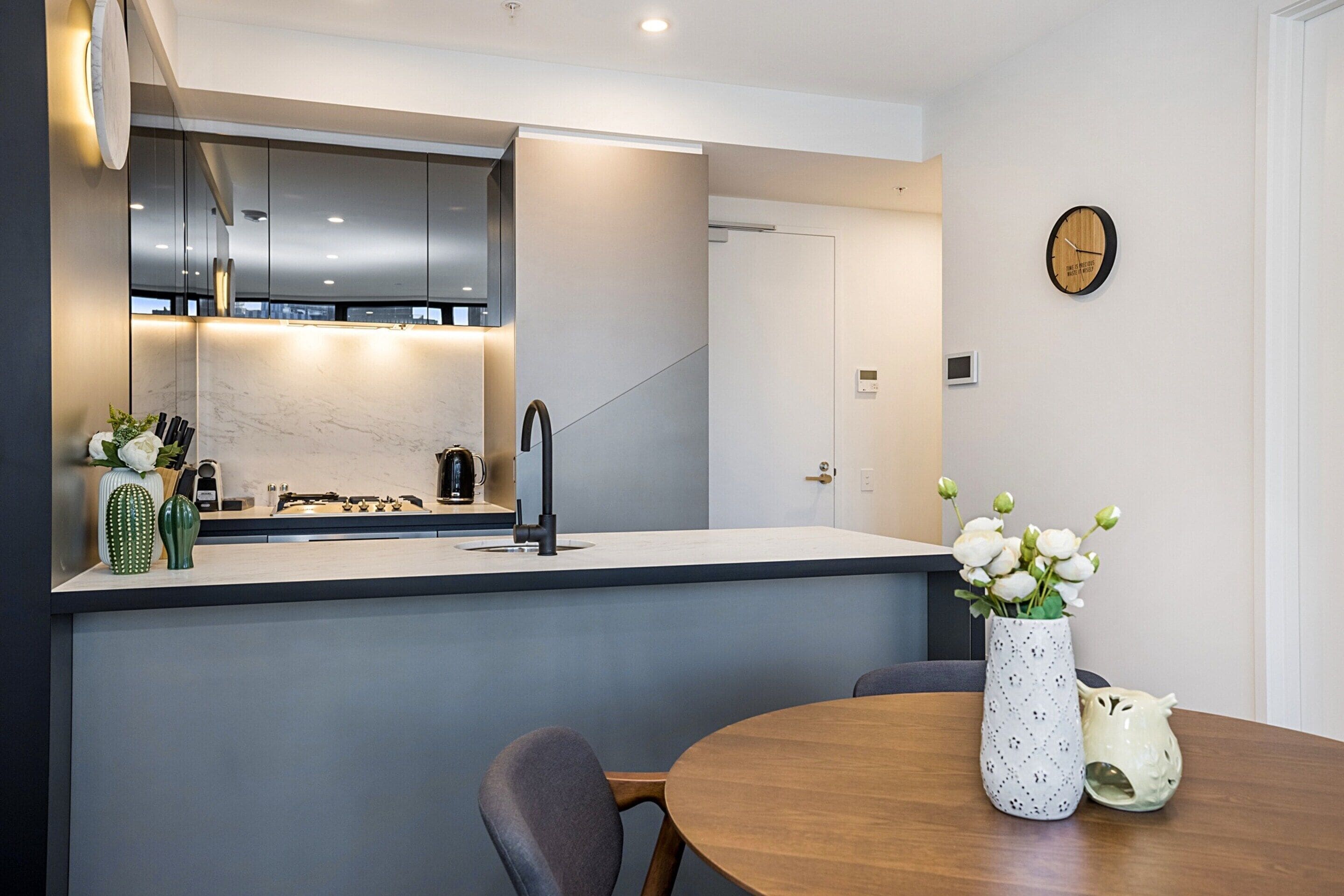 A modern kitchen with a built-in stove, dark cabinets, and a dining area with a wooden table and chairs.