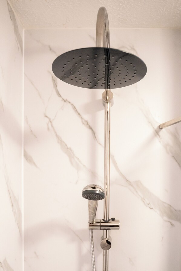 A modern shower with a rain showerhead and handheld showerhead against a marble wall.