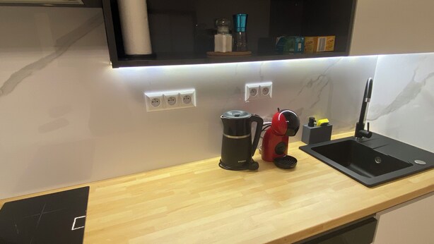 Una cocina moderna con encimera de madera, una cafetera negra, un hervidor rojo, un fregadero y un horno empotrado.