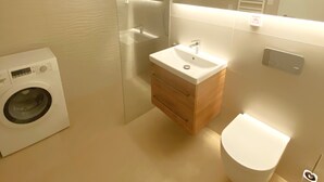 A modern bathroom with a built-in washing machine, a wooden vanity with a sink, and a toilet. - Apartment 10 min walk to center (Jihomoravský kraj)