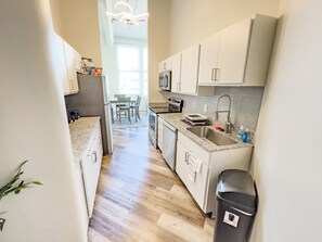 A modern kitchen with white cabinets, a granite countertop, a stainless steel sink, and a black trash bin. - Indy Apt, Skywalk Access, Gym & Private Parking (Indianapolis)