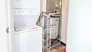 Uma lavanderia compacta com máquina de lavar e secadora brancas, um aquecedor de água e uma estante de metal.
