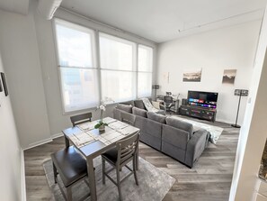 A modern living room with a grey sofa, a dining table with chairs, and a TV. - Indy Apt, Skywalk Access, Gym & Private Parking (Indianapolis)
