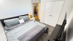Quarto com cama, mesa de cabeceira, televisão e guarda-roupa.