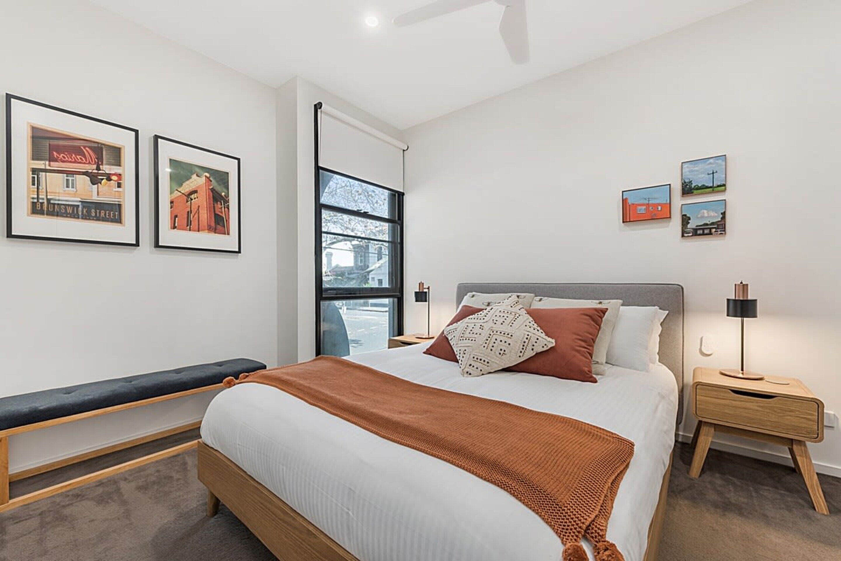 Quarto moderno com cama grande, um banquinho e quadros nas paredes.