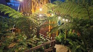 Une structure en bois surmontée d’un toit triangulaire, entourée d’une végétation luxuriante et accessible par un sentier.