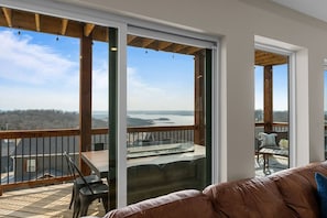 A balcony with a table and chairs, a leather couch, and a view of a body of water and forest. - Stunning view-Hot Tub-Game Room-Indoor Pool Access (Branson)