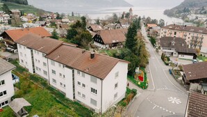 Een woongebied met moderne appartementencomplexen, een weg met een rotonde en een vergezicht op een meer en bergen.