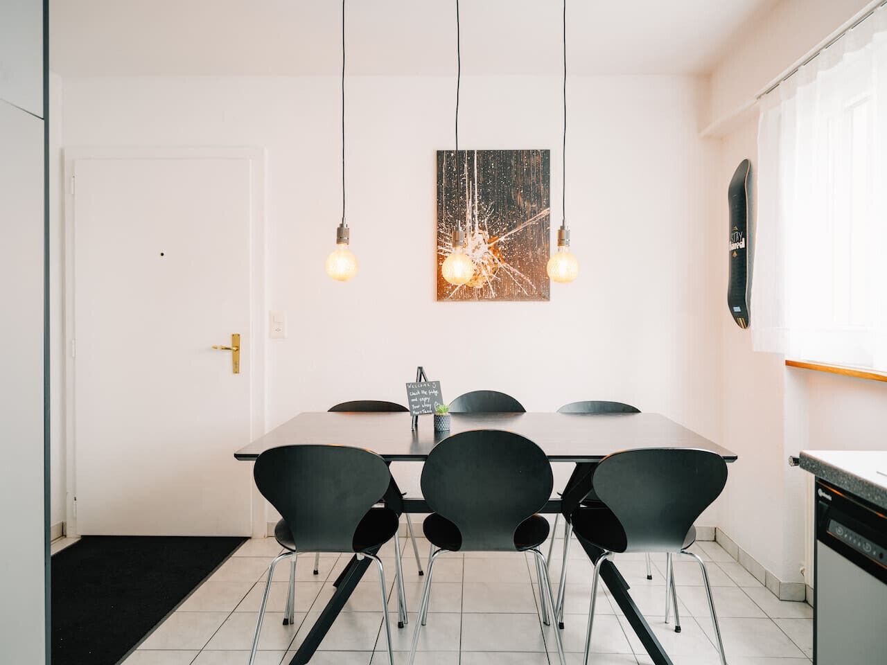 A modern dining area with a rectangular table, four black chairs, and pendant lights.