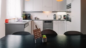 Een moderne keuken met witte kastjes, een zwarte eettafel en twee hangende pendelverlichting.