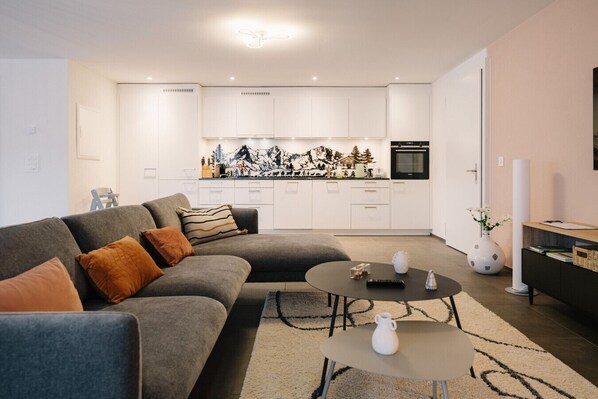 Un salon moderne avec un canapé gris, une table basse et une cuisine en arrière-plan.