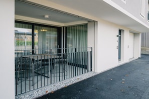 Un balcon avec une table et des chaises, une porte vitrée et la façade blanche d’un immeuble.
