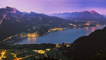 Paisagem montanhosa com um lago, estradas iluminadas e edifícios.